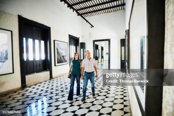 mature couple looking at artwork while walking through art gallery - couple museum foto e immagini stock