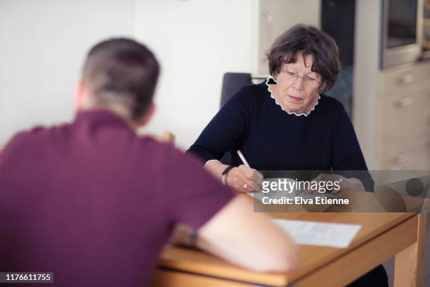older woman filling out forms on a dining table with her son - form filling stock pictures, royalty-free photos & images