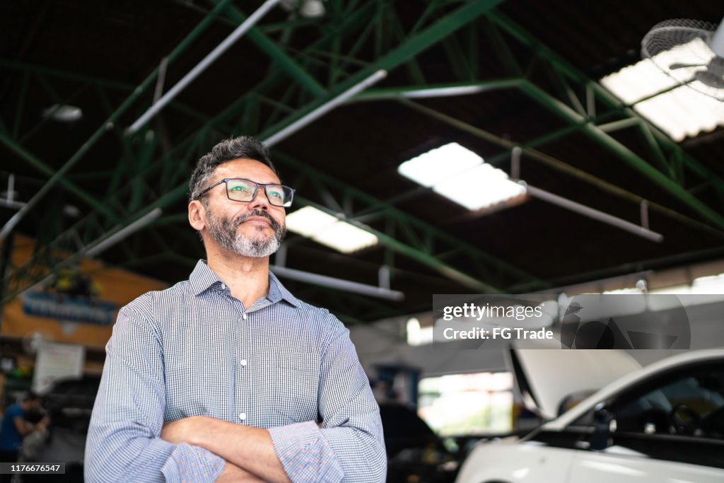 Man standing with arms crossed in a repair shop, looking away