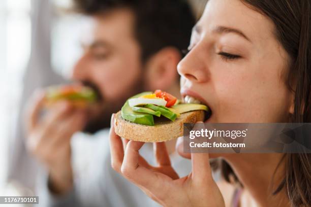 nahaufnahme von jungen frau beißen in ein sandwich - avocado stock-fotos und bilder