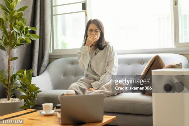 beautiful asian girl female a cough  and feeling sick with air pollution on cozy sofa with air purifier machine - air pollution photos et images de collection