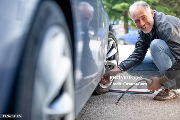 hombre maduro sonriente inflando neumáticos de coche al aire libre - inflar fotografías e imágenes de stock