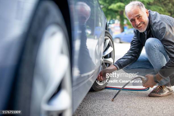 smiling mature man inflating car tires outdoors - tyres stock pictures, royalty-free photos & images
