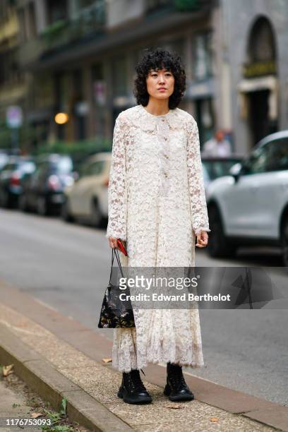 Guest wears a white lace long dress, a black brocade bag, black military-style boots, outside the Dolce & Gabbana show during Milan Fashion Week...