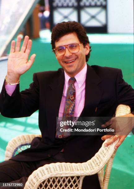 Italian tv-host Fabrizio Frizzi wave sat on a wicker arm-chair. 1990