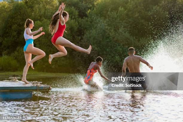 jeunes amis courant et sautant d'une jetée dans un lac - ponton photos et images de collection