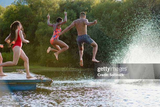 a group of friends jumping off a jetty into a lake - group-of-friends-jumping-off-dock-into-lake stock pictures, royalty-free photos & images