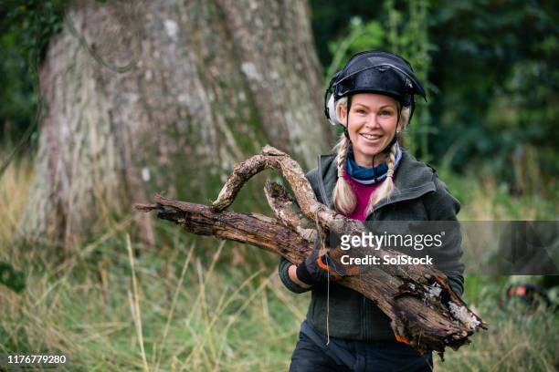 portrait of cheerful female tree surgeon carrying log - forester stock pictures, royalty-free photos & images