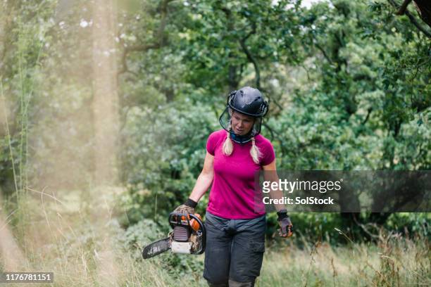 female tree surgeon wearing helmet and visor carrying chainsaw - chainsaw stock pictures, royalty-free photos & images