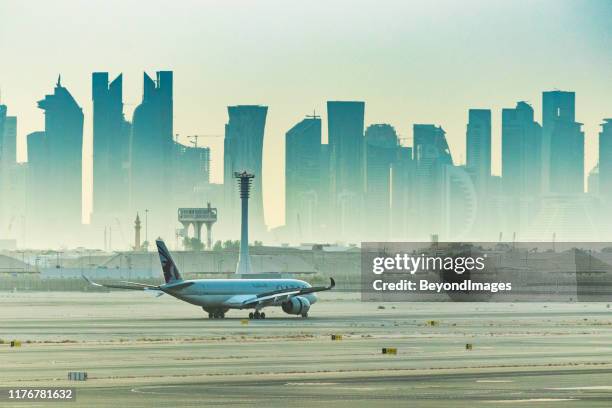 qatar airways flight preparing to depart hamad international airport with city skyline - doha airport stock pictures, royalty-free photos & images