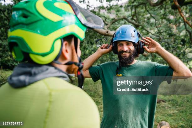 cheerful tree surgeon putting on ear defenders and smiling - ear defenders stock pictures, royalty-free photos & images