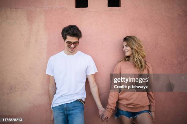 teenage couple holding hands and leaning on wall. - casal adolescente imagens e fotografias de stock