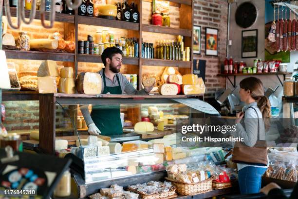 lateinamerikanische mann arbeitet in einem feinkostladen suggeting eine art von käse zu weiblichen kunden - food in market stock-fotos und bilder