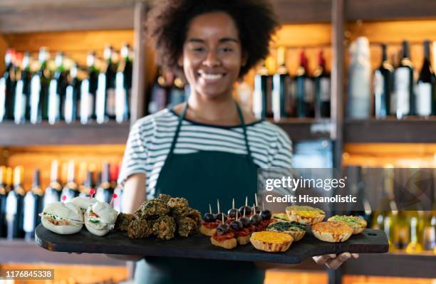 black cheerful waitress at a wine bar holding a tray of tapas smiling at camera - tapas stock pictures, royalty-free photos & images