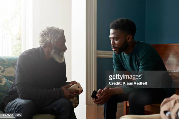male friends talking while sitting in living room - zoon stockfoto's en -beelden