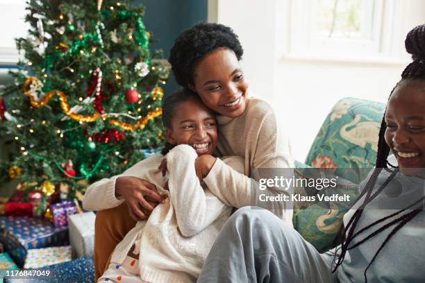 Smiling woman embracing girl while sitting on sofa