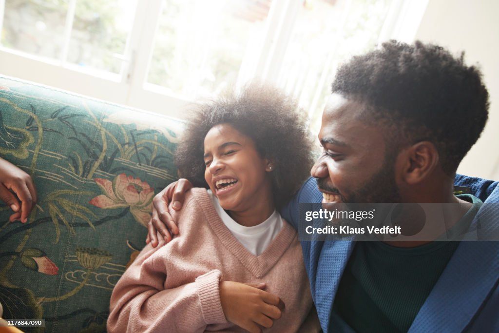 Young man embracing cheerful teenage girl on sofa