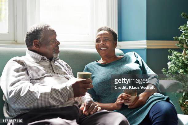 smiling senior couple talking on sofa at home - 2 cup of coffee stock pictures, royalty-free photos & images