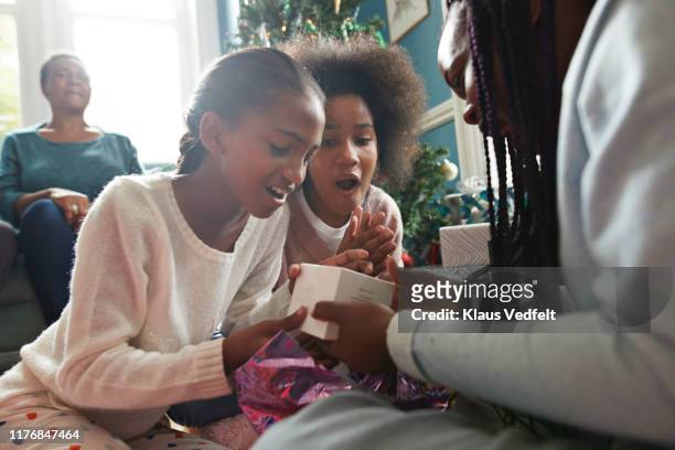 surprised sisters looking at christmas present - kerst cadeau meisje stockfoto's en -beelden
