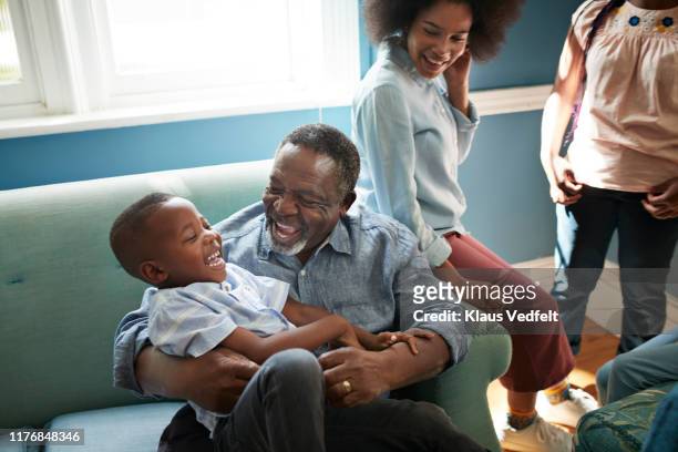 happy man playing with boy on sofa at home - grootouder stockfoto's en -beelden