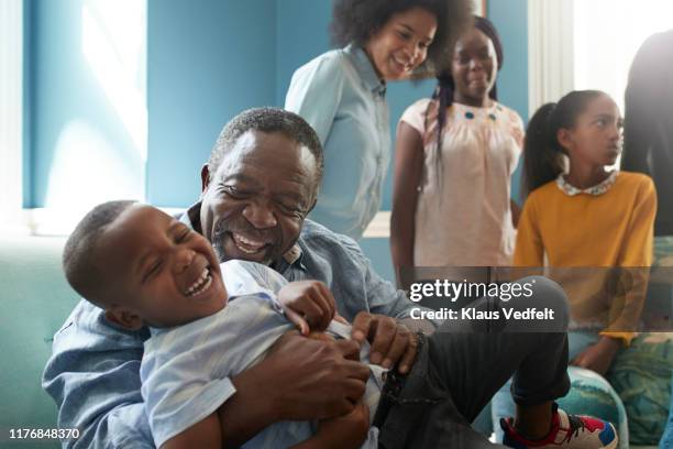 happy senior man playing with boy on sofa at home - african family stockfoto's en -beelden