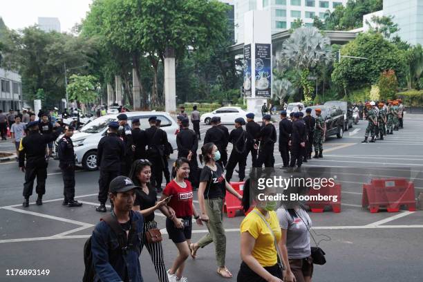 Pedestrians walk past police officers standing guard near the National Parliament complex ahead of the presidential inauguration in Jakarta,...