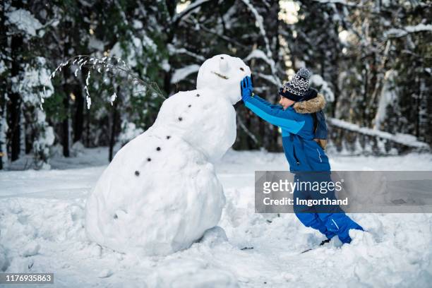 kleiner junge baut einen schneemann an einem wintertag - funny snow stock-fotos und bilder