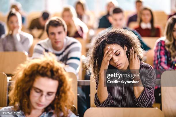 young university student having a headache on a class at lecture hall. - boring lecture stock pictures, royalty-free photos & images