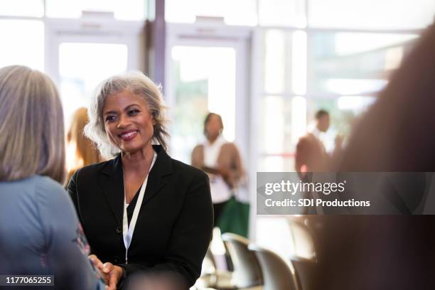attractive mature adult female conference speaker meets unrecognizable woman - diverse town hall meeting stock pictures, royalty-free photos & images