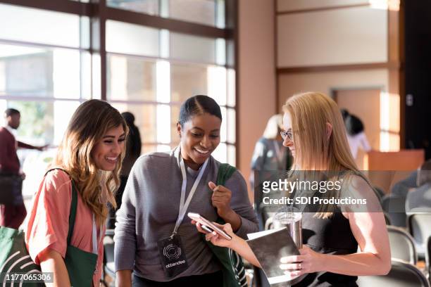 diverse women attending expo smile at smart phone photos - exhibition stock pictures, royalty-free photos & images