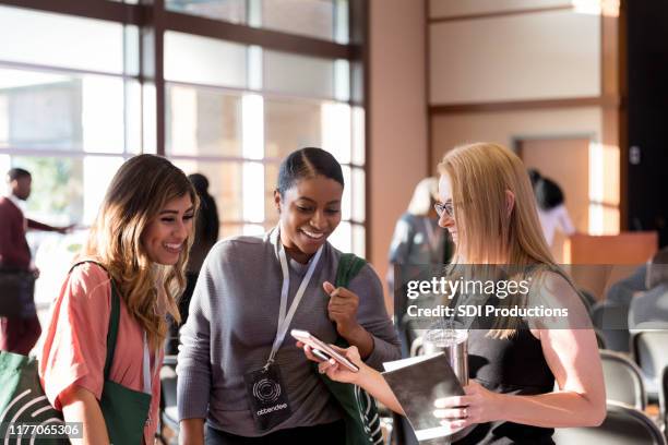 diverse women attending expo smile at smart phone photos - attending conference stock pictures, royalty-free photos & images