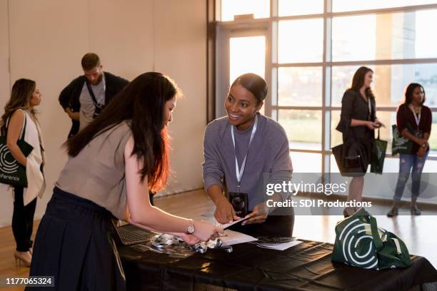 mid adult woman explains expo events in brochure to attendee - exhibition stock pictures, royalty-free photos & images