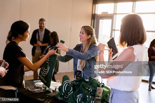 mid adult woman hands out conference tote bags - tote bag stock pictures, royalty-free photos & images