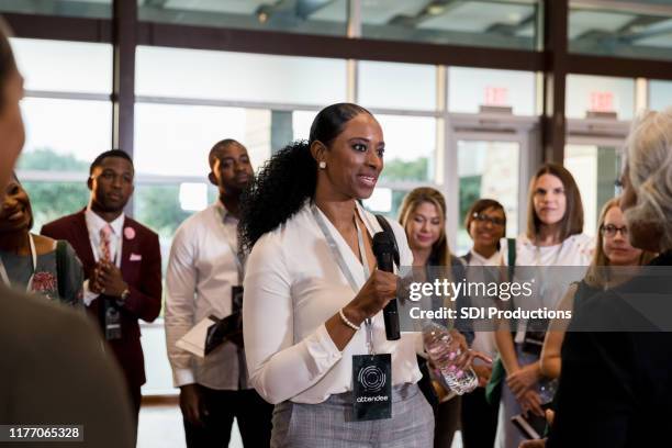 mid adult woman with microphone asks expo speaker question - diverse town hall meeting stock pictures, royalty-free photos & images