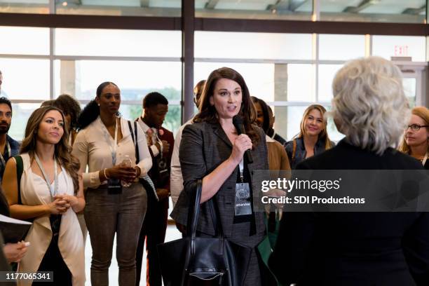 mid adult woman asks unrecognizable speaker question - diverse town hall meeting stock pictures, royalty-free photos & images