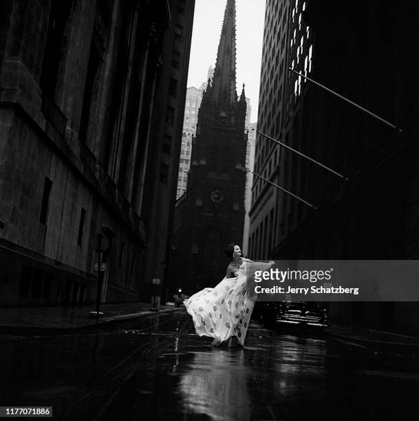 Dressed in a white dress with black polka dots and white gloves, American fashion model Betsy Pickering takes a spin on Wall Street , New York, New...