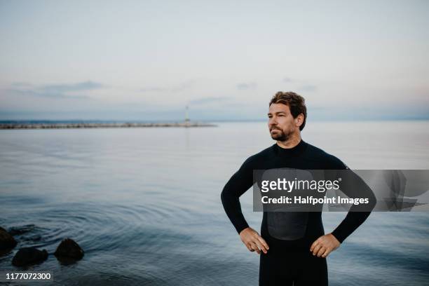 a fit mature sportsman with wetsuit standing outdoors on beach, a copy space. - neoprene fotografías e imágenes de stock