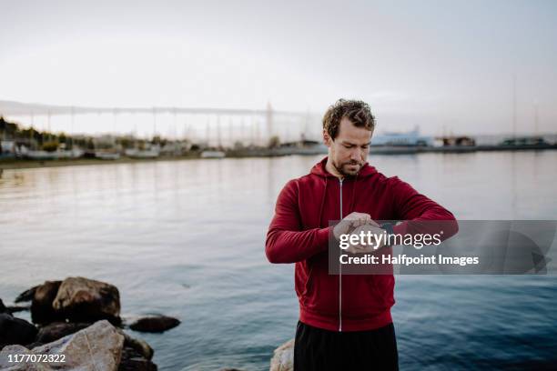 a fit mature sportsman runner standing outdoors on beach, using smartwatch. - checking sports fotografías e imágenes de stock