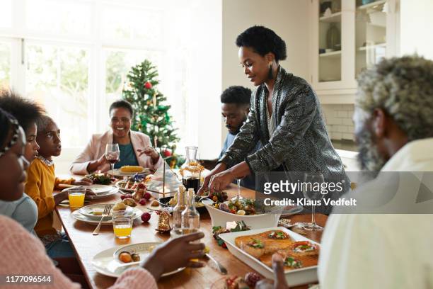 woman serving food to friends and family at home - holiday dinner stock-fotos und bilder