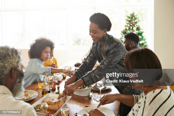 young woman serving food to friends and family - happy family eating photos et images de collection