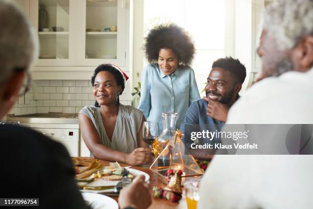 smiling friends and family talking at home - african at dining table stockfoto's en -beelden