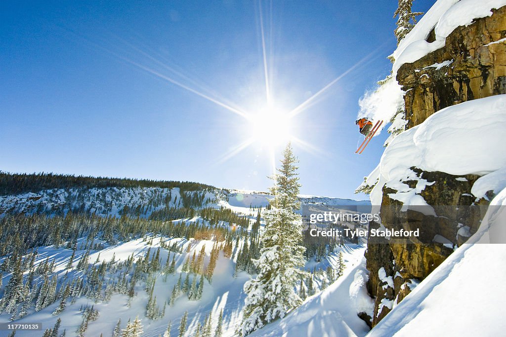 Skier jumping cliff on sunny winter day.