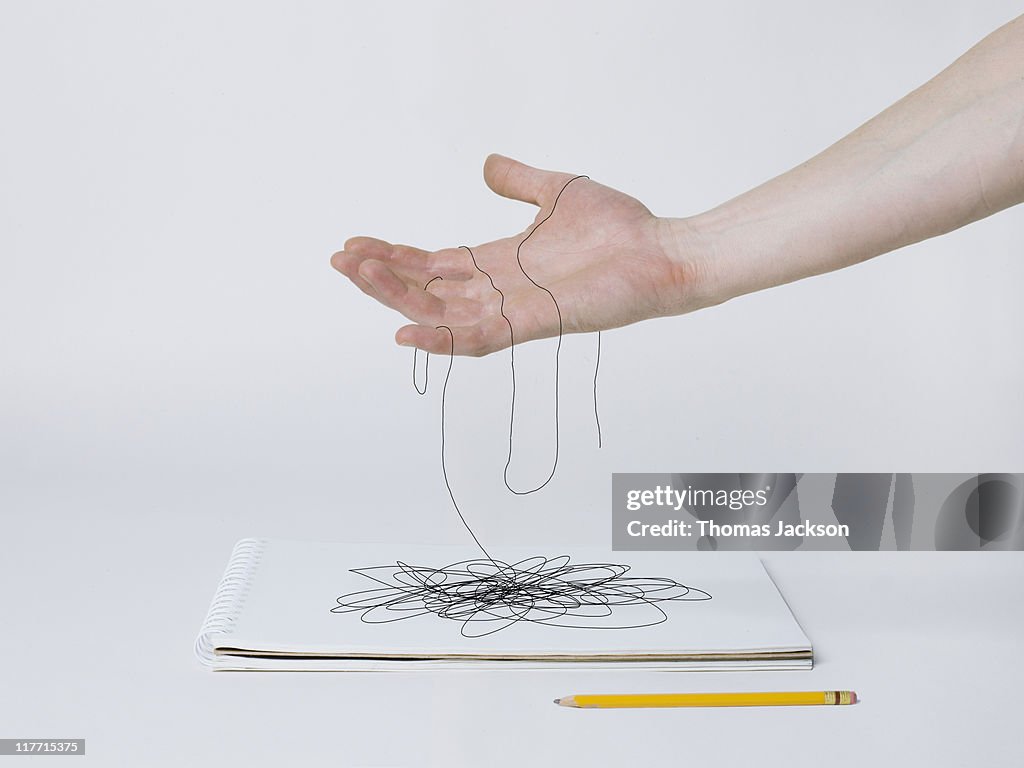 Hand holding pencil lines that turn into thread