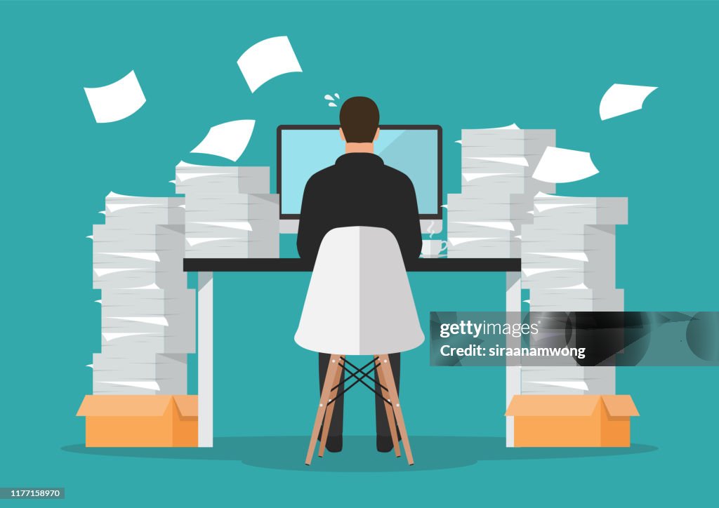Busy businessman working on computer with pile of papers