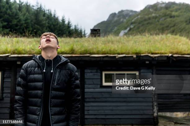 teenage boy looking skywards standing in front of grass roofed black cottage - zwart jak stockfoto's en -beelden