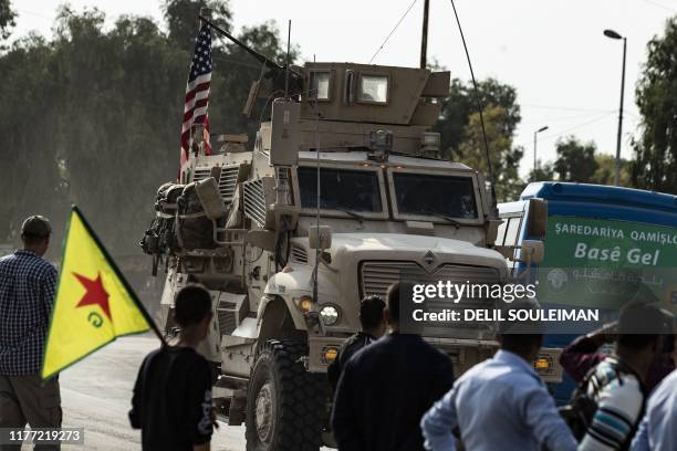Syrian Kurds, one of them carrying a Kurdish YPG flag, watch as a US military vehicle drives on a road after US forces pulled out of their base in...