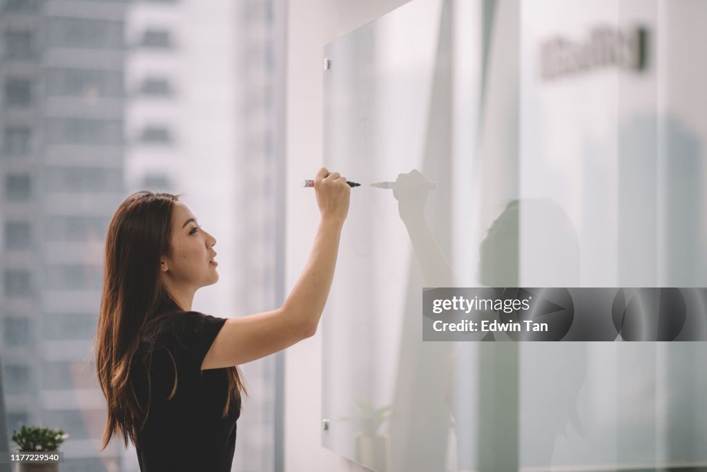 Una mujer china asiática escribiendo en la pizarra blanca con su rotulador durante la reunión de la conferencia en la sala de conferencias de la oficina