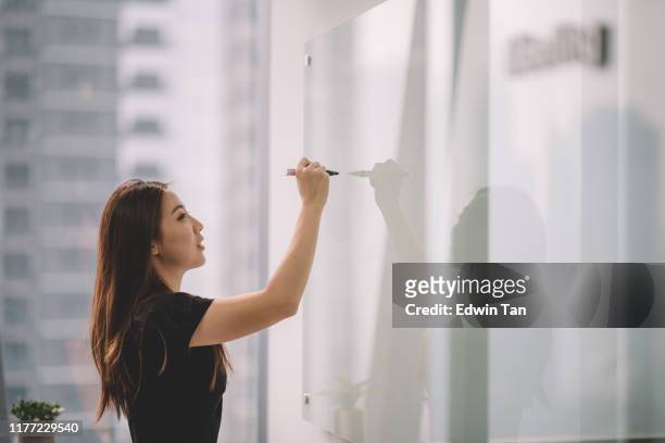 una donna cinese asiatica che scrive su lavagna bianca con la pennarello durante la riunione della conferenza nella sala conferenze dell'ufficio - determinazione foto e immagini stock