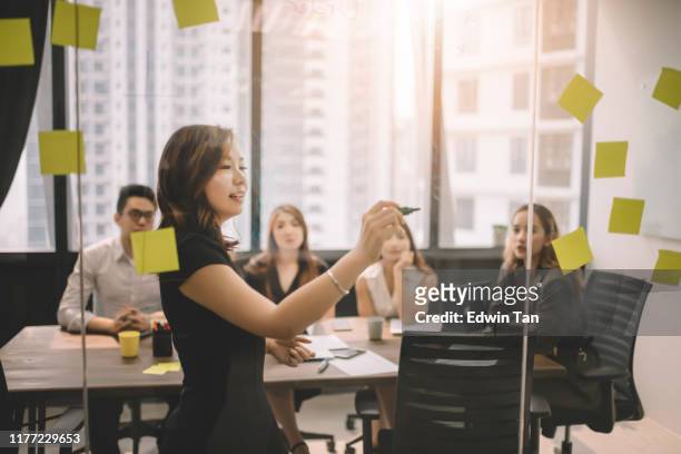 un grupo de colegas asiáticos que tienen discusión en la sala de reuniones con pegatina amarilla en la ventana lluvia de ideas jugando con ideas - asia fotografías e imágenes de stock