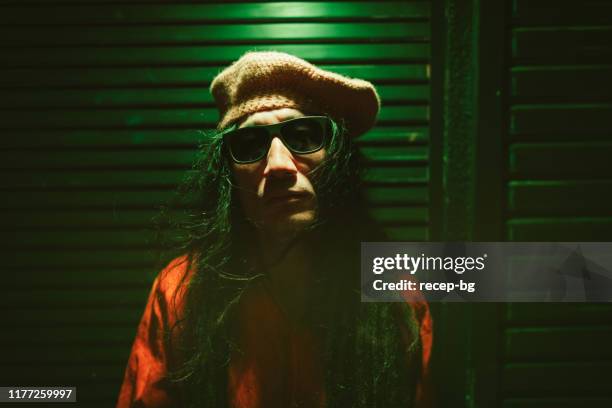 porträt des mannes mit dreadlocks von neonfarbenen lichtern in der nacht beleuchtet - grüner hut stock-fotos und bilder